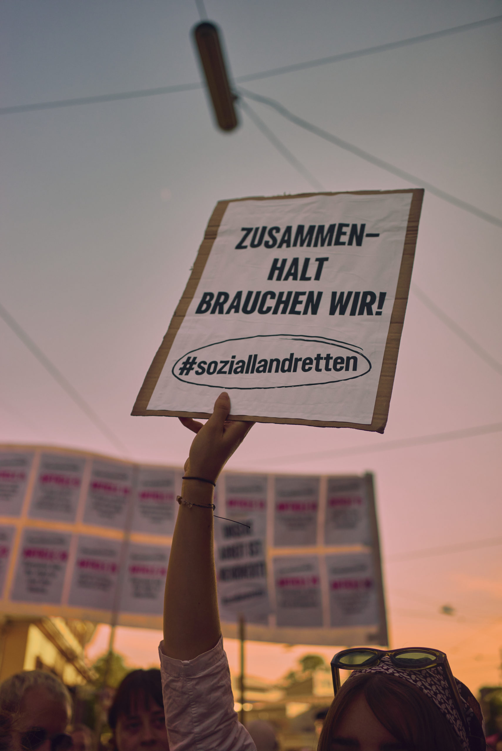 Person hält Schild hoch mit dem Spruch: Zusammenhalt brauchen wir! #soziallandretten